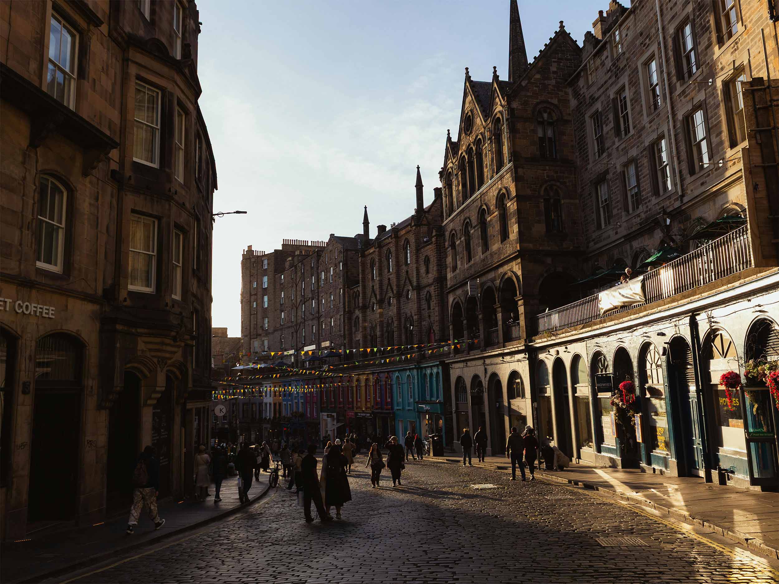 A photo of one of Edinburgh&amp;amp;#39;s iconic Victoria Street in dusk, showing people milling about under streetlights